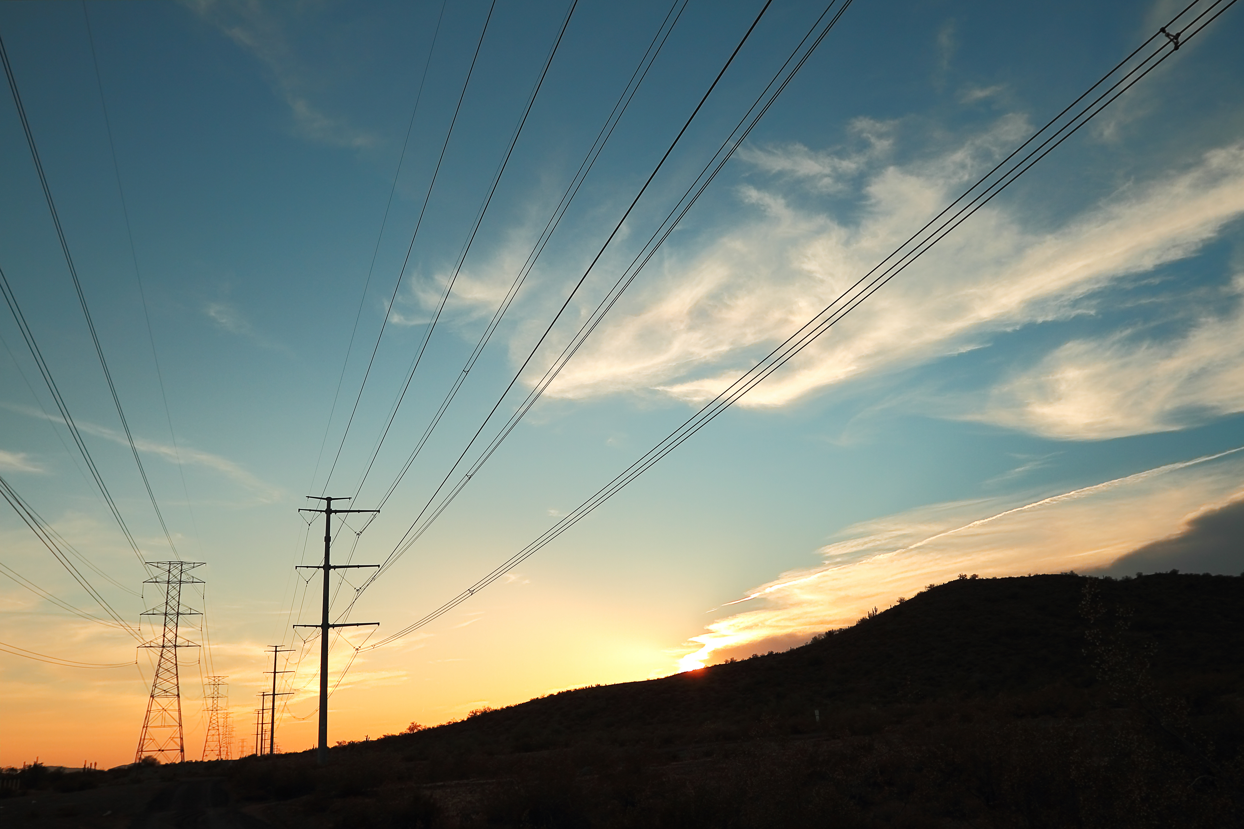 Power transmission towers at sunset Power transmission pylons silhouetted against a blue and orange sky